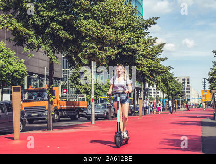 Jeune femme équitation E-scooter sur le Boulevard des étoiles, Berlin, Allemagne Banque D'Images