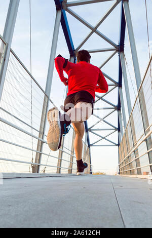 Jogger avec le smartphone dans la poche du bras tournant sur un pont Banque D'Images