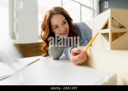 Portrait of smiling redheaded woman looking at architectural model Banque D'Images