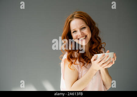 Portrait de femme rousse heureux avec bol de céréales contre l'arrière-plan gris Banque D'Images