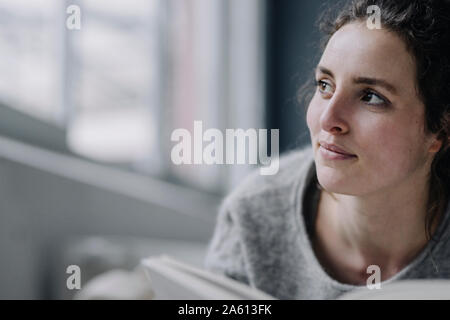 Portrait de jeune femme détendue avec livre à la maison Banque D'Images