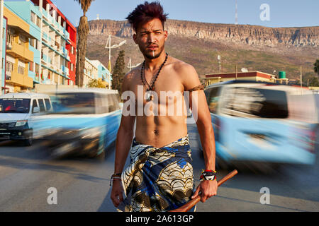 L'homme Tribal avec son arc et flèches traditionnelles au milieu de la ville avec des voitures qui passent, Lubango, Angola Banque D'Images