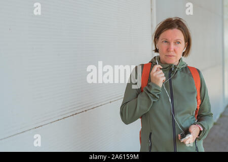Female jogger talking on mobile téléphone en mode mains libres pendant que la marche vive la rue Banque D'Images