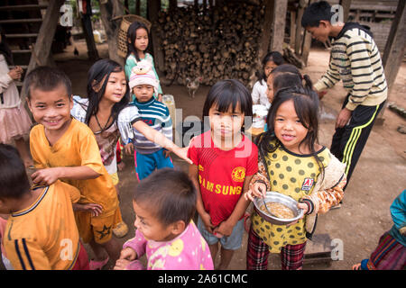 Les enfants d’un village de Khmu au Laos se réunissent autour d’une table, profitant d’une collation partagée et de moments joyeux ensemble. Banque D'Images