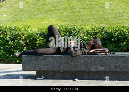 Beyoglu, Turquie - 20 octobre 2019 : Young African man with baseball hat et des vêtements noirs dormir sur un banc en béton au parc public à Istanbul Banque D'Images