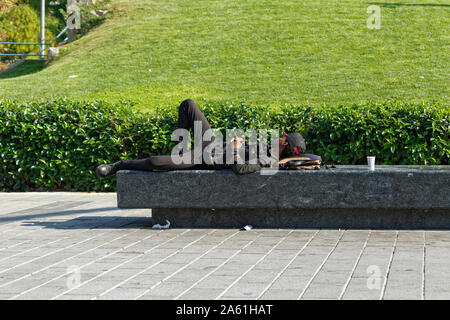 Beyoglu, Turquie - 20 octobre 2019 : Young African man with baseball hat et des vêtements noirs dormir sur un banc en béton au parc public à Istanbul Banque D'Images