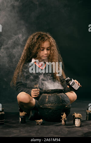 Portrait d'un mignon petit magicien femelle avec de magnifiques longs cheveux bruns vêtu d'un pull bleu marine, gris jupe, chaussettes et chaussures. Elle est sit Banque D'Images