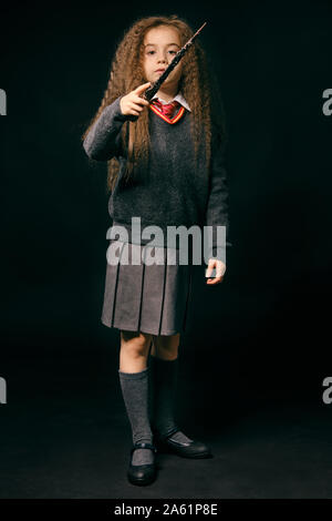 Portrait d'une magnifique petite fille sorcière avec de magnifiques longs cheveux bruns vêtu d'un pull bleu marine, gris jupe, chaussettes et chaussures. Elle est hol Banque D'Images