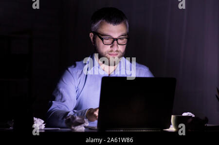 Puzzled man looking at laptop screen in dark room Banque D'Images