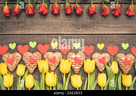 En forme de cœur avec des fleurs et des coeurs en papier coloré gingerbreads créez un cadre avec une copie, l'espace. Tulipes jaunes odorantes, roses rouges avec des bonbons. Banque D'Images