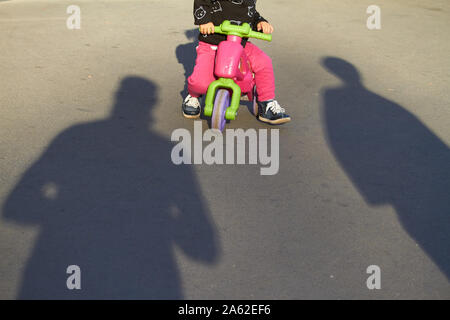 Kharkiv, Ukraine - le 14 octobre 2019 : un enfant sur un vélo de l'enfant et l'ombre de parents sur le trottoir Banque D'Images