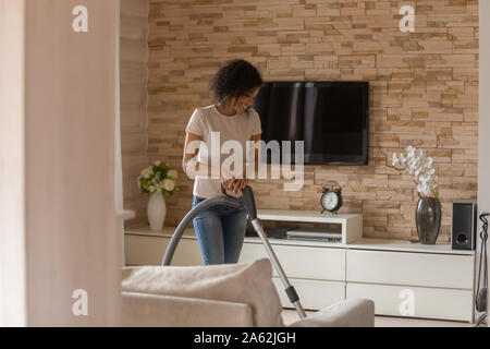 Happy young african american woman à l'aide d'aspirateur sur le tapis. Banque D'Images