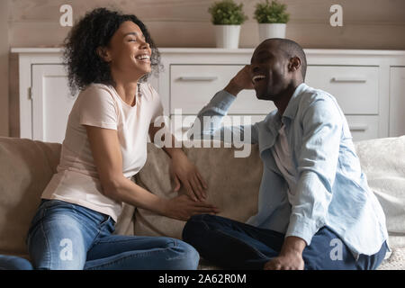 African American millénaire heureux couple sitting on sofa, à bavarder. Banque D'Images