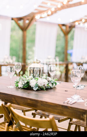 Décorations de mariage dans un style rustique sur table en bois, arrangement floral et de golden lantern. Tableau servis avec des couverts et de la vaisselle, wineglasses. Banque D'Images