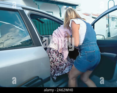 Une aide soignant un frêle vieille dame sur le siège de la voiture afin qu'elle puisse s'asseoir dans un fauteuil roulant par la suite. Selectiv focus shot. Banque D'Images