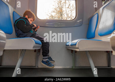 Garçon avec un téléphone mobile assis en train. Les enfants et les technologies. Jeune garçon joue une partie sur le téléphone tout en restant assis dans le train. La qualité de connexion internet. Jeune voyageur Voyages avec la carte électronique Banque D'Images