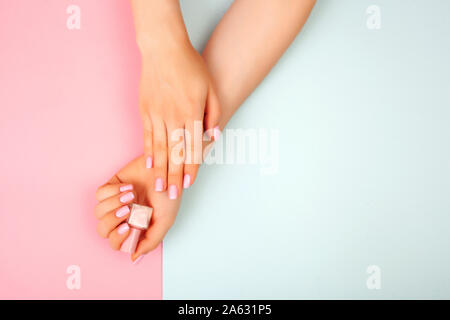 Mode femme élégante manucure. Belle jeune femme avec ses mains avec du vernis à ongle sur fond rose et bleu. Banque D'Images