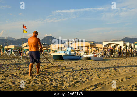 Un homme mûr de derrière mitraillant le sable d'une plage de Lido di Camaiore sur la côte de la Versilia au coucher du soleil en été, Toscane, Italie Banque D'Images