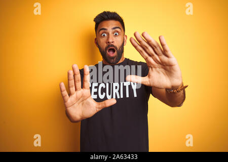 Sauvegarde hispanique indienne arabe homme portant un uniforme de sécurité sur fond jaune isolé peur et terrifié par la peur expression geste arrêter wit Banque D'Images