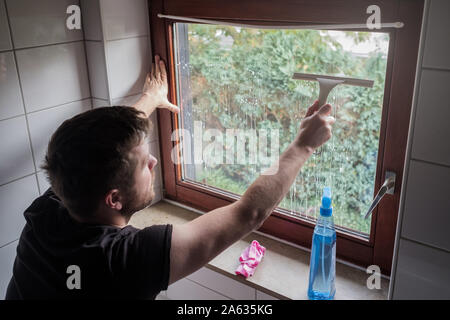 L'homme se lave une fenêtre dans une chambre d'utilisation d'une raclette Banque D'Images