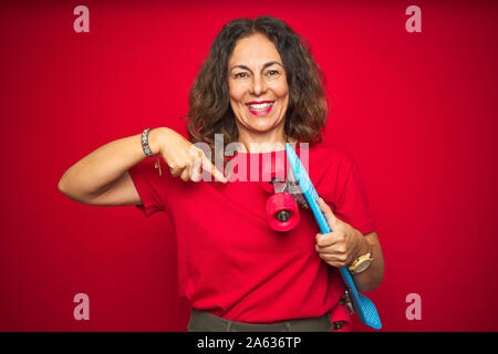 L'âge moyen du patineur senior woman holding skateboard rouge sur fond isolé avec surprise face à face à lui-même Banque D'Images