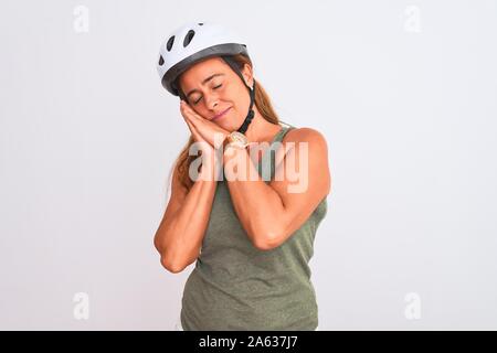 L'âge moyen cycliste mature femme portant un casque de sécurité sur fond isolé fatigué dormir rêver et posant avec les mains tout en souriant wi Banque D'Images