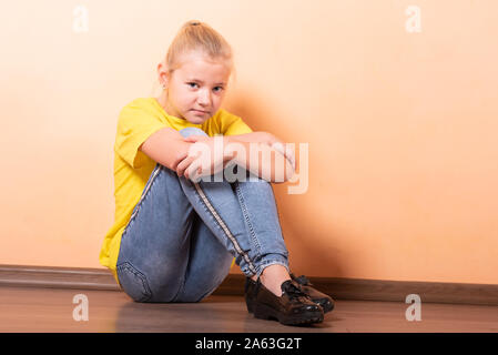 Girl sitting offensé sur le sol, la lumière fond orange. Banque D'Images