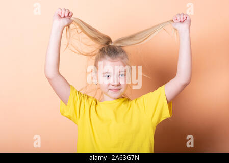 Une fille tire elle-même par les cheveux sur un fond orange. Banque D'Images