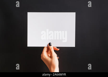 Woman's hand with black nailpolish tenant un papier blanc sur le fond noir. Banque D'Images