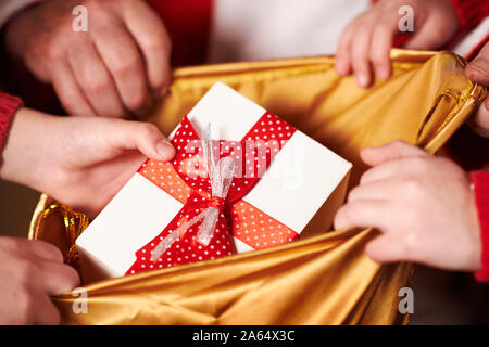 Le Père Noël ouvre un sac et donne des cadeaux aux enfants, assis près de l'arbre de Noël décoré avec des lumières - Joyeux Noël et bonnes fêtes ! Banque D'Images