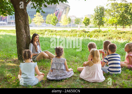 Les enfants occupent une leçon avec le professeur dans le parc sur une pelouse verte Banque D'Images