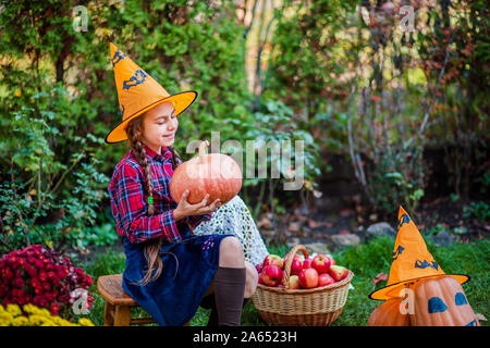 Cute little girl hugs une citrouille dans le jardin d'automne. La célébration de la récolte d'automne. Banque D'Images