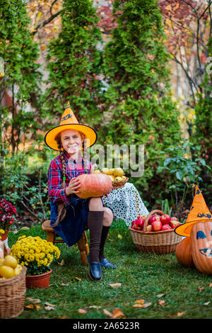 Cute little girl hugs une citrouille dans le jardin d'automne. La célébration de la récolte d'automne. Banque D'Images