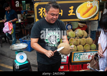 24.02.2019, Singapour, République de Singapour, en Asie - Un vendeur coupe ouvrir un durian frais avec un couteau sur un marché de rue dans le quartier chinois. Banque D'Images