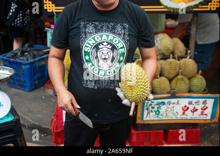 24.02.2019, Singapour, République de Singapour, en Asie - Un fournisseur est titulaire d'un durian frais et un couteau à la main au cours d'un marché de rue dans le quartier chinois. Banque D'Images