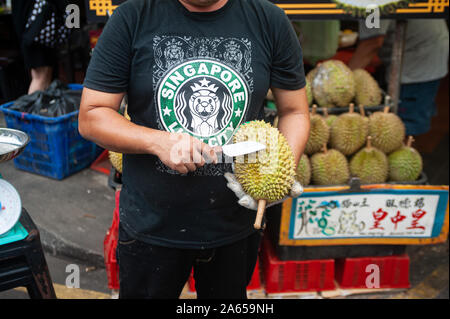 24.02.2019, Singapour, République de Singapour, en Asie - Un fournisseur est titulaire d'un durian frais et un couteau à la main au cours d'un marché de rue dans le quartier chinois. Banque D'Images