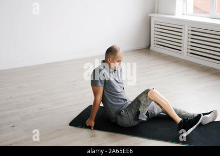 Jeune homme à la jambe artificielle assis sur les tapis d'exercice et de repos après l'entraînement sportif Banque D'Images