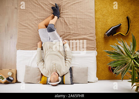 Portrait de jeune homme handicapé dans les écouteurs couché sur le lit et écouter de la musique dans la chambre à coucher Banque D'Images