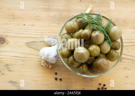 Tomates cerises vertes aigre à l'aneth dans une plaque de verre sur un fond de bois avec de l'ail et poivre noir Banque D'Images