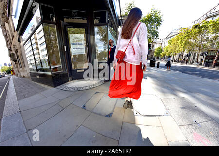 Londres, Angleterre, Royaume-Uni. Jeune femme en blanc top et jupe rouge dans le Strand Banque D'Images