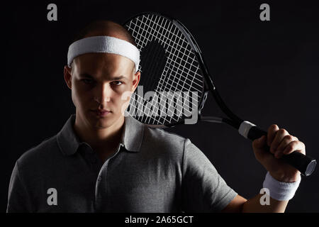 Studio shot of young sportsman avec racket à l'encontre de l'appareil photo à l'arrière-plan noir Banque D'Images