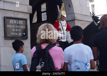 Un soldat de la reine des maîtres nageurs en Horse Guards Parade, Whitehall, Londres, avec une mère et ses deux fils l'observation Banque D'Images