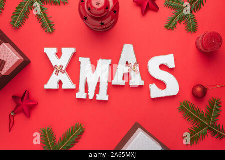 Lettres décoratives de noël entouré de décorations de Noël et des cadeaux. Noël, Nouvel An composition sur surface rouge. Mise à plat, vue du dessus. Banque D'Images