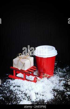 Café pour aller à red cup, un traîneau et cadeau de Noël sur fond noir. Boissons chaudes en hiver froid. Noël et Nouvel An. Banque D'Images