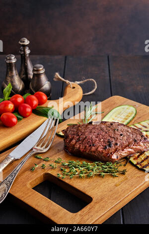 Pavé de boeuf servi avec des courgettes et tomates fraîches et basilic cerise sur planche à découper en bois Banque D'Images