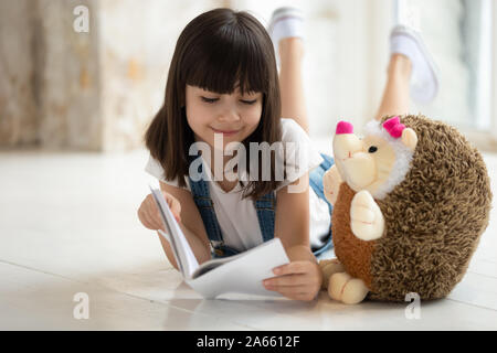 Adorable girl laying on marbre chaud avec ses jouets préférés, lecture. Banque D'Images