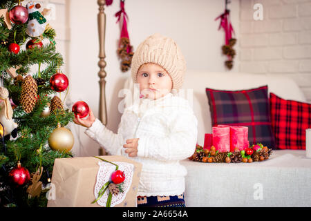 Little girl decorating Christmas Tree, canapé avec coussins en arrière-plan. Banque D'Images