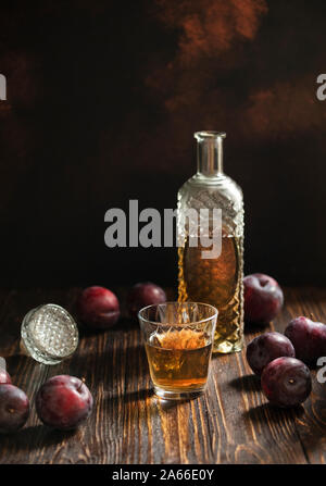 Rakia ou traditionnels de fruits brandy rakija des Balkans. Eau-de-vie de prune sljivovica dans un verre et la carafe sur une table en bois et un arrière-plan sombre. La verticale Banque D'Images