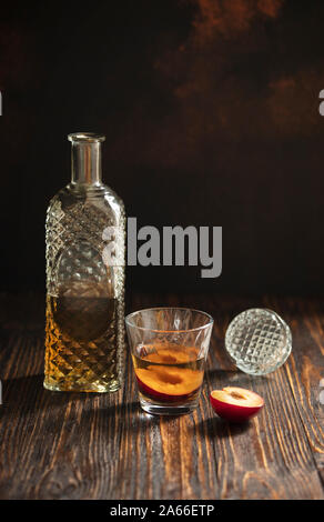 Rakia ou traditionnels de fruits brandy rakija des Balkans. Eau-de-vie de prune sljivovica dans un verre et la carafe sur une table en bois et un arrière-plan sombre. La verticale Banque D'Images