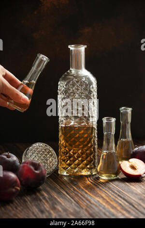 Rakia ou traditionnels de fruits brandy rakija des Balkans. Eau-de-vie de prune slivovica dans un verre qui s'appelle cokanj et bouteille sur une table en bois Banque D'Images